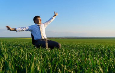 İş adamı bir alanda ofis koltuğunda oturur ve dinlenir, serbest ve iş konsepti, arka plan olarak yeşil çimenler ve mavi gökyüzü