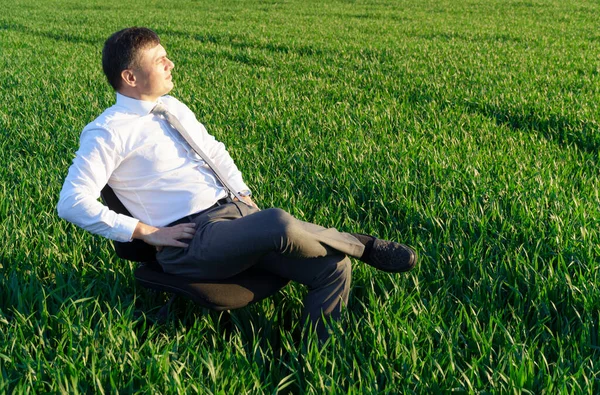 商人坐在田野里的办公椅上休息 自由职业和商业概念 绿草和蓝天作为背景 — 图库照片