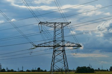 Mavi gökyüzüne karşı yüksek voltajlı elektrik hatları, kuleler ve endüstriyel altyapı
