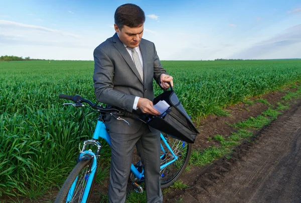 自転車を持つビジネスマンは 緑の芝生のフィールドでブリーフケースから文書を取ります またはフリーランスのためのビジネスコンセプト 美しい春の自然 — ストック写真