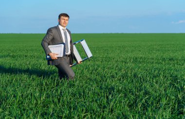 İş adamı yeşil bir alanda poz veriyor. Belge ve merdiven, serbest ve iş konsepti, arka plan olarak yeşil çimen ve mavi gökyüzü ile devam ediyor.