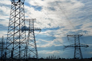 Mavi gökyüzüne karşı yüksek voltajlı elektrik hatları, kuleler ve endüstriyel altyapı