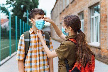 Okul çocuğu ve liseli kız okula giderken yüzlerinde koruyucu bir maskeyle Coronavirus enfeksiyonu, eğitim ve okula dönüş konseptine karşı poz veriyorlar.