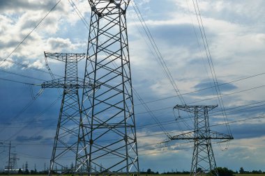 Mavi gökyüzüne karşı yüksek voltajlı elektrik hatları, kuleler ve endüstriyel altyapı
