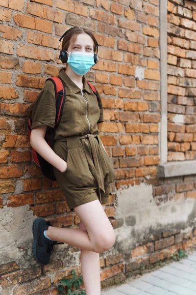 女子高生は学校の裏庭にあるレンガの壁にポーズをとり コロナウイルス感染症から顔に保護マスクを着用し 教育を受け 学校のコンセプトに戻る — ストック写真
