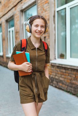 Okula giden genç bir liseli kız. O, kulaklıkla müzik dinliyor ve bir kitap tutuyor. Eğitim ve okul konseptine dönüş