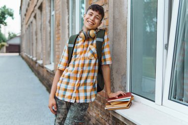 Okula giderken, kitaplarla, eğitimle ve okul konseptiyle poz veren mutlu genç çocuk portresi.