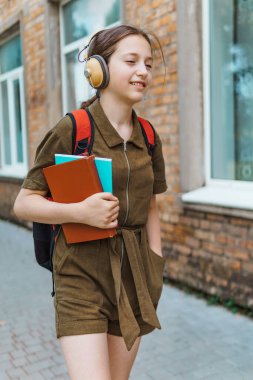 Okula giden genç bir liseli kız. O, kulaklıkla müzik dinliyor ve bir kitap tutuyor. Eğitim ve okul konseptine dönüş