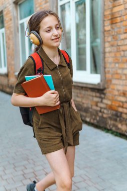 Okula giden genç bir liseli kız. O, kulaklıkla müzik dinliyor ve bir kitap tutuyor. Eğitim ve okul konseptine dönüş