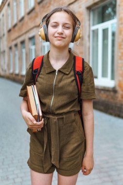 Okula giden genç bir liseli kız. O, kulaklıkla müzik dinliyor ve bir kitap tutuyor. Eğitim ve okul konseptine dönüş