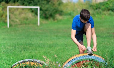 Delikanlı dışarıda spor yapıyor, bahçede spor yapıyor, bağcıklarını bağlıyor ve ısınıyor, sağlıklı bir yaşam sürüyor.