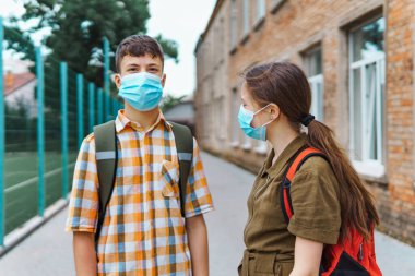 Okul çocuğu ve liseli kız okula giderken yüzlerinde koruyucu bir maskeyle Coronavirus enfeksiyonu, eğitim ve okula dönüş konseptine karşı poz veriyorlar.
