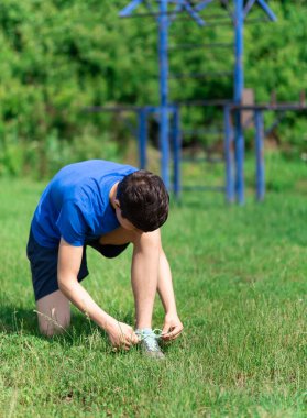 Delikanlı dışarıda spor yapıyor, bahçede spor yapıyor, bağcıklarını bağlıyor ve ısınıyor, sağlıklı bir yaşam sürüyor.