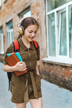 Okula giden genç bir liseli kız. O, kulaklıkla müzik dinliyor ve bir kitap tutuyor. Eğitim ve okul konseptine dönüş