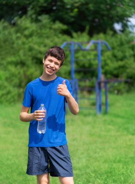 Delikanlı dışarıda spor yapıyor, bahçede spor yapıyor, bir şişe su ve içecek açıyor, sağlıklı bir yaşam tarzı.