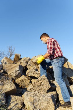 Bir adam taş yığını ve kırık beton parçalarıyla çalışır, inşaat enkazı taşır.