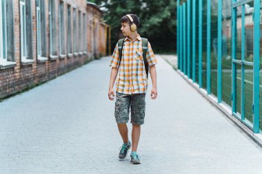 Okula giderken mutlu genç portresi, kulaklıkla müzik dinliyor, eğitim ve okul konseptine geri dönüyor.