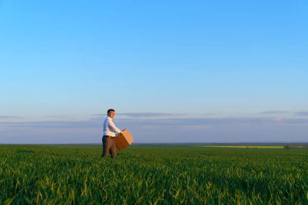 ビジネスマンは 段ボール箱を保持し 緑の芝生のフィールドにポーズ ビジネスコンセプト — ストック写真