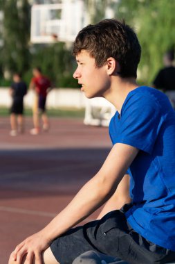 Adam sahanın kenarında oturuyor ve basketbol maçı seyrediyor.