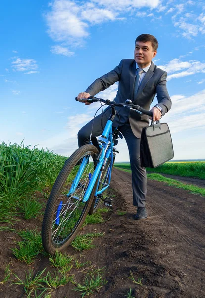 ビジネスマンは緑の芝生のフィールドで自転車に乗る 休暇やフリーランスのためのビジネスコンセプト 美しい春の自然 — ストック写真