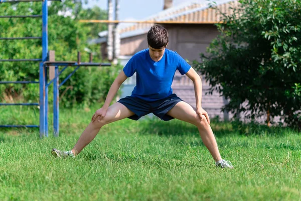 Tonårspojken Tränar Utomhus Idrottsplats Gården Han Knäböjer Och Gör Uppvärmning — Stockfoto