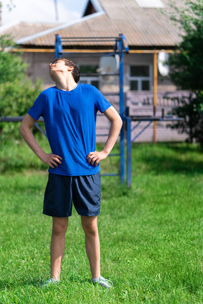 teenage boy exercising outdoors, sports ground in the yard, he does a warm-up, healthy lifestyle