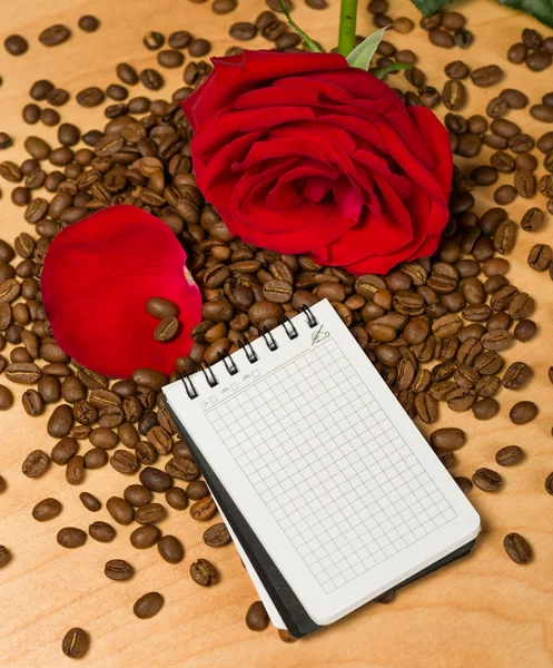 赤いバラとコーヒーの種子と木製の背景ノート — ストック写真