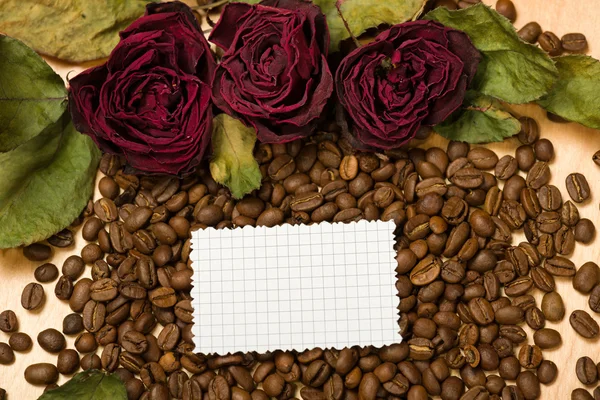 Rosas rojas secas y hoja de papel en blanco sobre semillas de café y fondo de madera — Foto de Stock