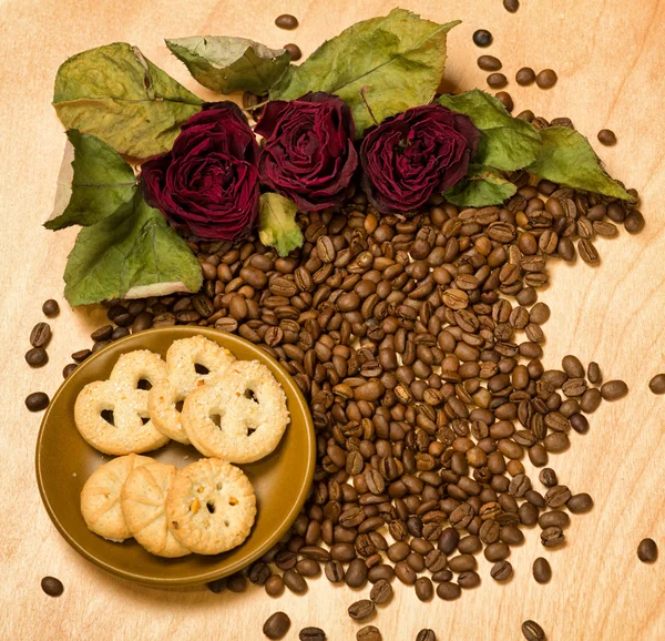 Rosas rojas secas y galletas sobre semillas de café y fondo de madera — Foto de Stock