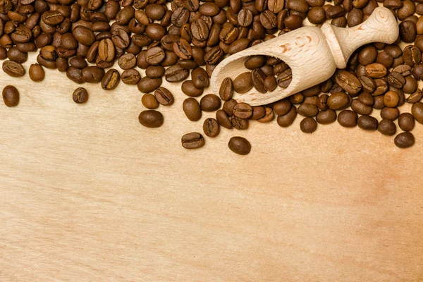 Coffee seeds with wooden shovel on wood background — Stock Photo, Image