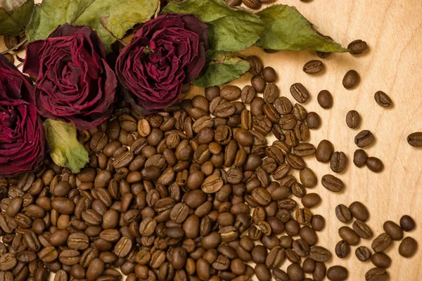 Dry red roses on coffee seeds and wooden background — Stock Photo, Image