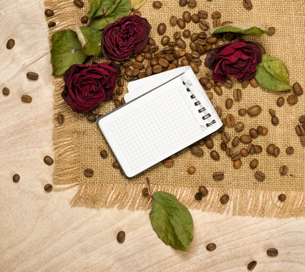 Leeres Blatt und trockene rote Rosen auf Kaffeesamen — Stockfoto