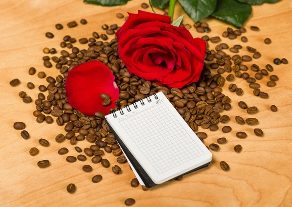 Červená růže a notebook na kávy semen a dřevěné pozadí — Stock fotografie