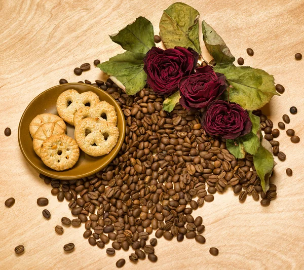 Trockene rote Rosen und Kekse auf Kaffeesamen und Holzhintergrund — Stockfoto