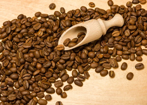 Coffee seeds with wooden shovel on wood background — Stock Photo, Image