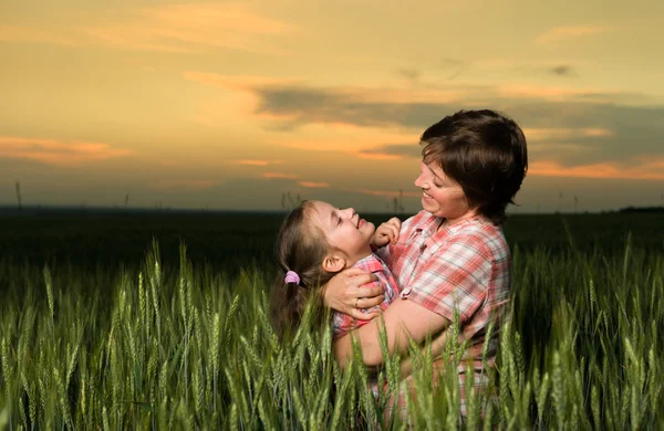 Mãe feliz e criança no campo verde ao pôr do sol — Fotografia de Stock