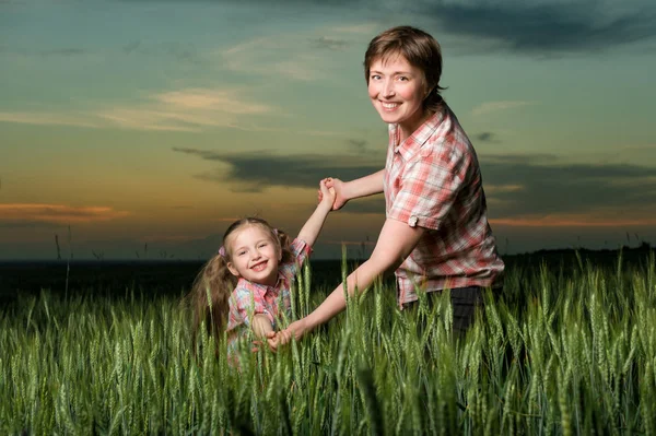 Šťastné matky a dítěte v zeleném poli při západu slunce — Stock fotografie