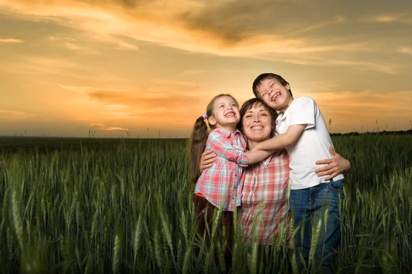 Gelukkig moeder en childs in groene veld bij zonsondergang — Stockfoto