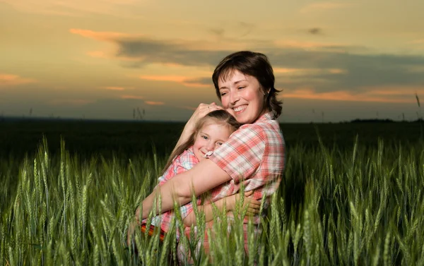 Šťastné matky a dítěte v zeleném poli při západu slunce — Stock fotografie