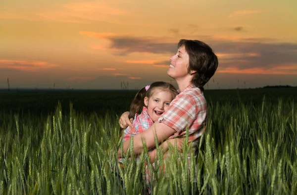 Gelukkig moeder en kind in groene veld bij zonsondergang — Stockfoto