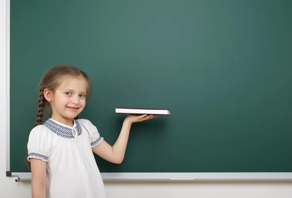 Schoolmeisje met boek in de buurt van schoolbestuur — Stockfoto