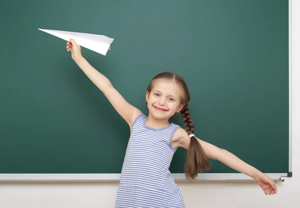 Schoolmeisje met papier vliegtuig in de buurt van schoolbestuur — Stockfoto
