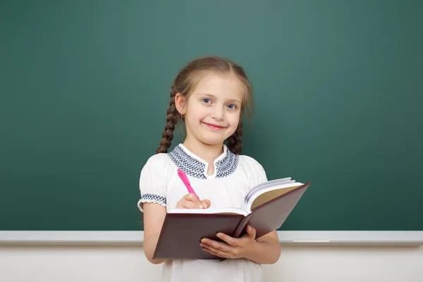 Colegiala con libro cerca de la junta escolar — Foto de Stock