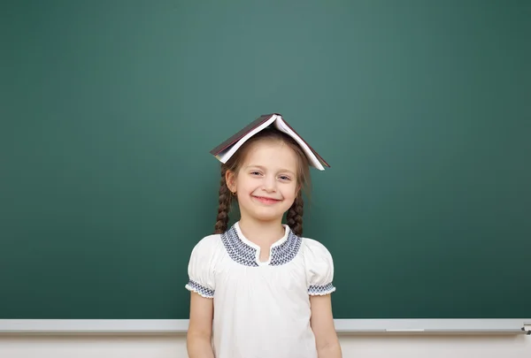 Schoolmeisje met boek in de buurt van schoolbestuur — Stockfoto