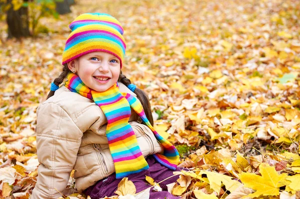 Meisje zitten op bladeren van de herfst in park — Stockfoto