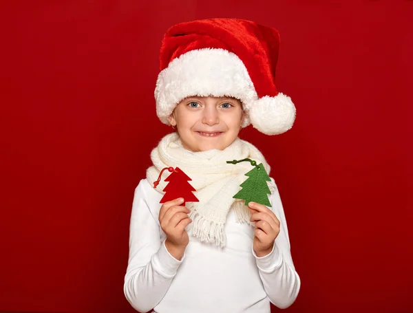 Winter, child,  christmas concept - happy girl in santa hat show fir tree wool toy on red — ストック写真