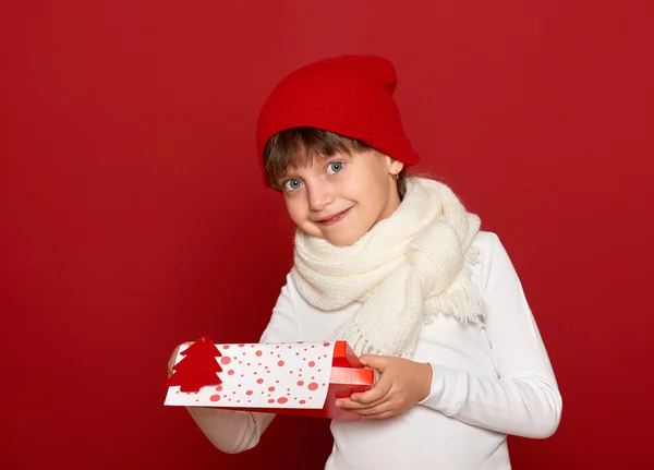 Inverno, criança, conceito de natal - menina feliz no chapéu com caixa de presente mostrar brinquedo de lã de abeto no vermelho — Fotografia de Stock