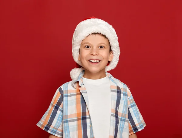 Winter holiday christmas concept - boy in santa hat portrait on red background — Stock Photo, Image