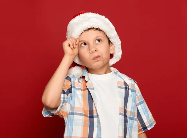 winter holiday christmas concept - boy in santa hat have idea on red background