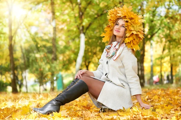 Fille s'asseoir sur les feuilles dans le parc de la ville d'automne — Photo